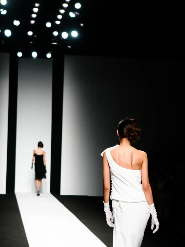 Model in white one-shoulder dress on a fashion runway.